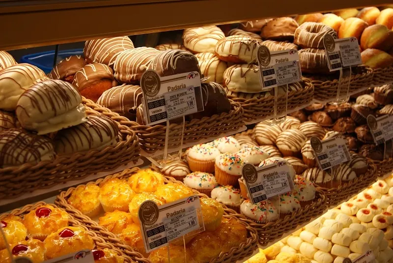 Cestas de pães e doces numa vitrine de padaria, cada uma com etiqueta de preço em pé num suporte transparente fino